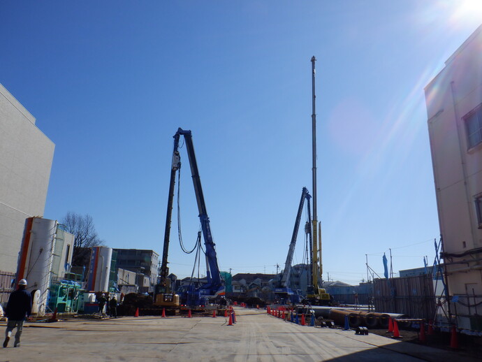 写真: 工事現場に二台の工事車両が入っています。杭を入れるための穴を掘っています。